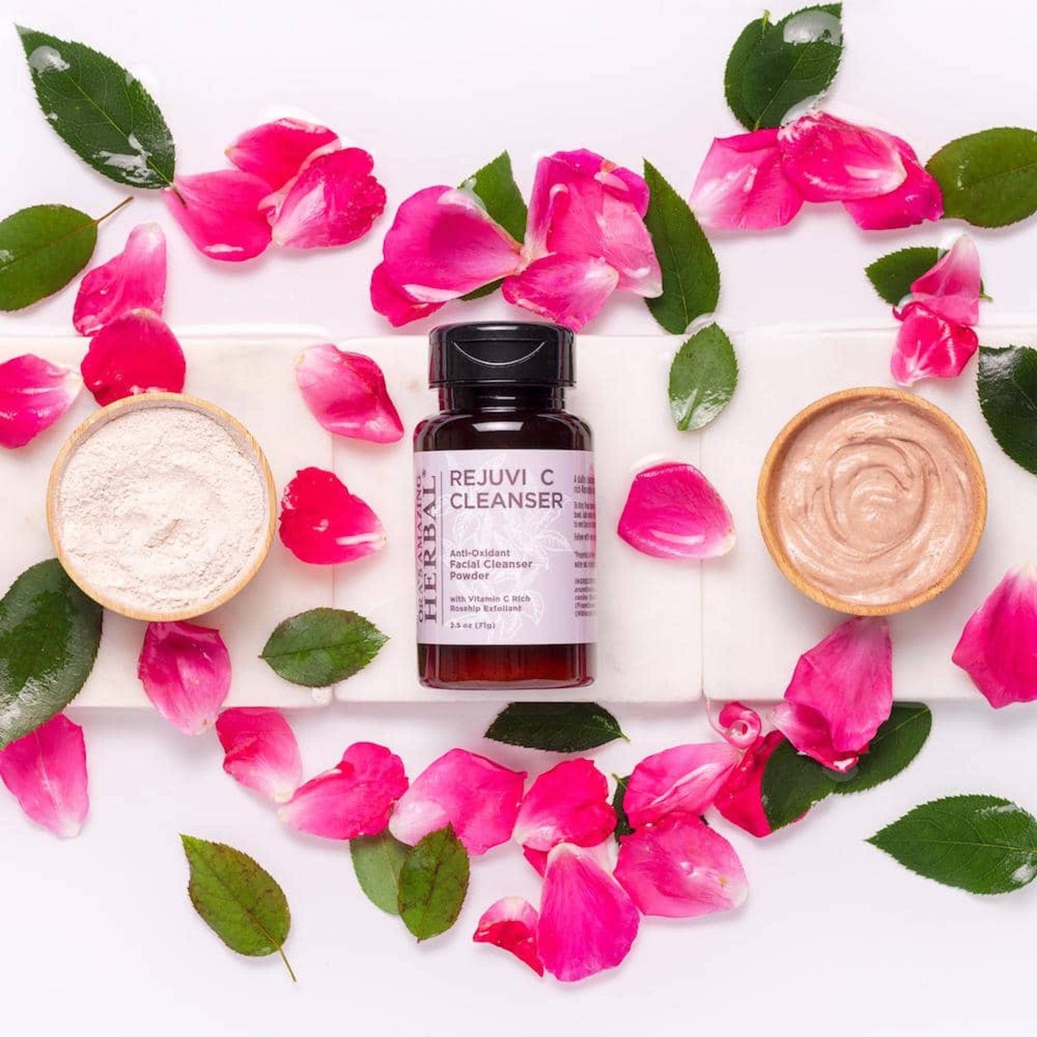 Facial Cleanser powder with Ora's Amazing Herbal bottle, pink rose petals, and wooden bowls on white surface
