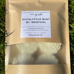 Shower steamers in a brown paper bag with clear window, By Rubie label, and white tablets inside