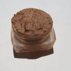 Close-up of golden brown loose powder eyeshadow with shimmer particles in a small glass jar