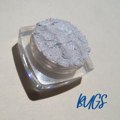 Side view of two loose glitter eyeshadow pigments in white and silver shades with reflective sparkle, showcasing texture