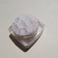 Close-up of sparkling white loose eyeshadow with violet shimmer particles in a circular jar