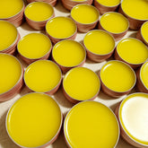 Lip balms, yellow glossy balm in round metal tins, arranged in a grid pattern