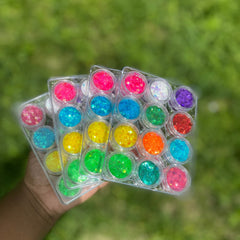 Twelve iridescent glitter pots in rainbow hues arranged in a circular display with shimmering particles visible