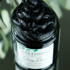 Hand scooping charcoal cleansing balm from black jar, showing rich texture for detoxifying skincare routine