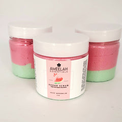 Sugar scrub jars with pink and green layers, white lids, and Ameelah Essentials label