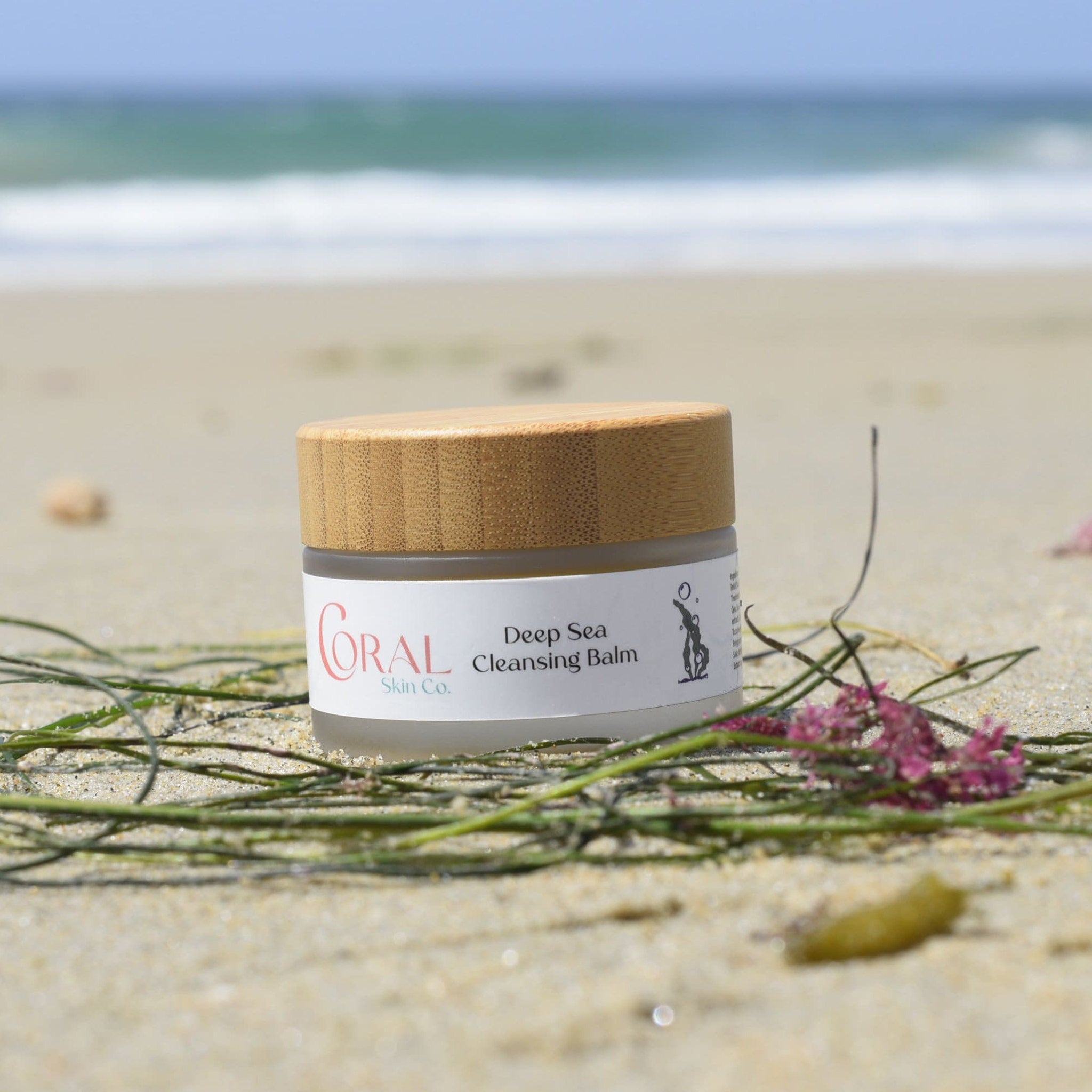 Facial cleanser jar with wooden lid, glass body, and Coral Skin Co. label on beach