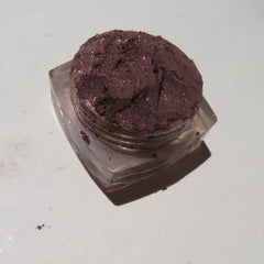 Close-up of loose dark brown shimmer eye shadow with fine mineral particles in a glass jar