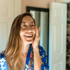 Woman smiling with long brown hair, wearing a blue floral patterned robe, touching face