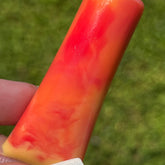 Lip gloss, red and orange swirl, held by a hand against a green background