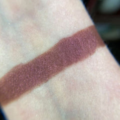 Close-up of a hand applying shimmery taupe eye shadow with a fluffy blending brush for a soft, diffused look.