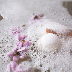 Bath bomb in white with pink flower petals and bubbles, in bath water