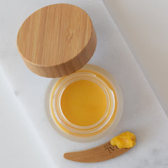 Balm jar with wooden lid, yellow balm, and wooden spatula on white surface