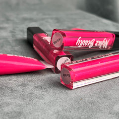 Lip gloss tubes in bright pink with black caps and Nyiaz Beauty branding on a grey surface