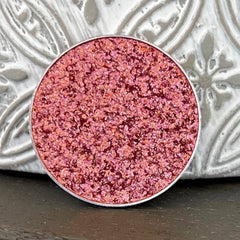 Pink glitter eyeshadow with silver rim, close up view on a dark surface.