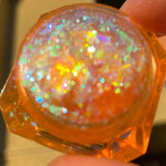 Close-up of multichrome flakes being applied to eyelid with fingertip, showing iridescent color shift