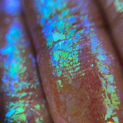 Close-up of multichrome eye shadow flakes shifting between teal, purple, and gold hues