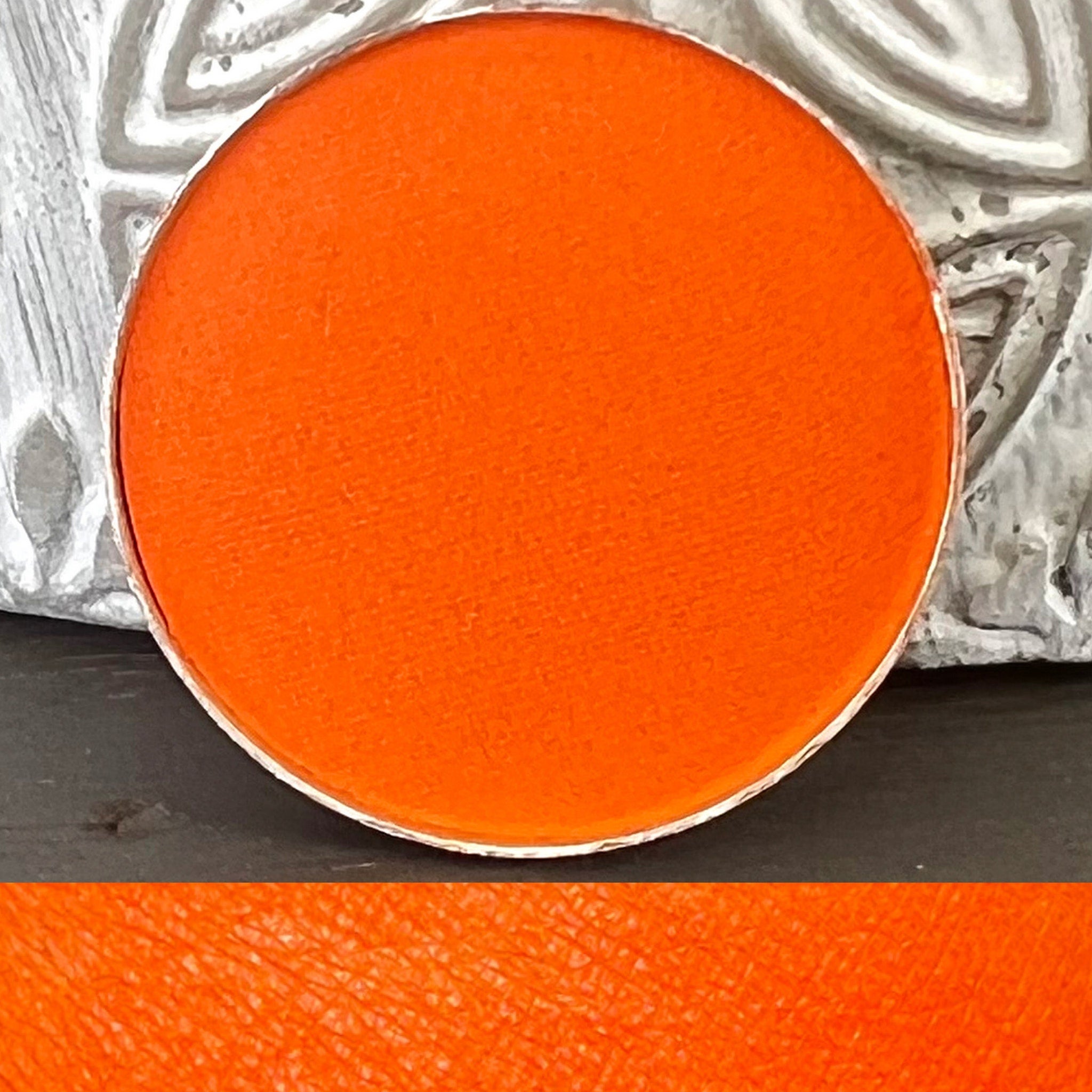 Eyeshadow pan, bright orange matte, metallic silver rim, circular shape