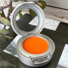 Eyeshadow compact with orange pigment, silver metal casing, and reflective mirror lid