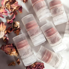 Tinted lip balm in clear tubes with pink balm and "All Day" text, rose petals around
