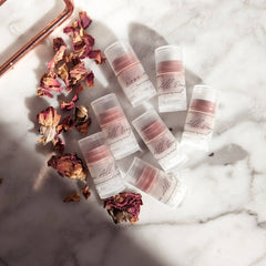 Tinted lip balm tubes with pink balm, clear plastic, and "All Day" text on marble surface