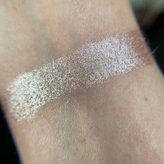 Side view of shimmery champagne eye shadow pot catching light with elegant metallic packaging