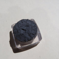 Black powder in clear plastic container, on light background, shadow visible