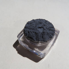 Dark gray powder in clear square container on white surface with shadow