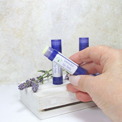 Lavender lip balm in blue tube with white label, held by hand with lavender sprig in background