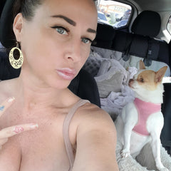 Woman with gold earrings, pink lips, and dog in car with pink harness