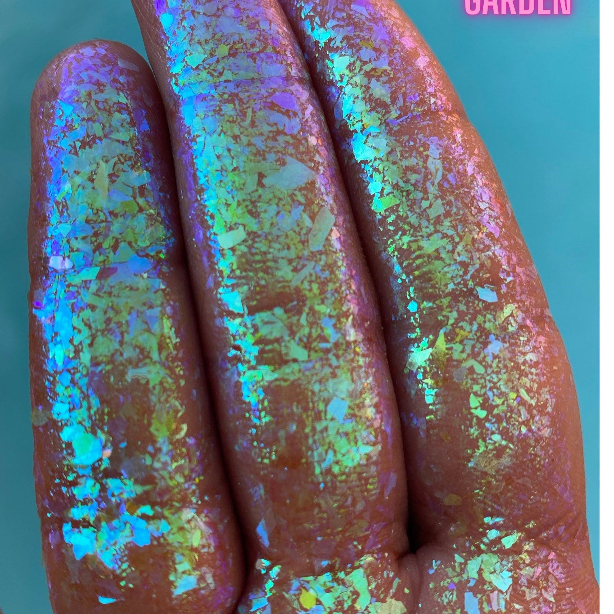 Close-up of Triton’s Garden multichrome eye shadow flakes shifting between teal, purple, and gold hues in circular pan.