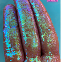 Close-up of Triton’s Garden multichrome eye shadow flakes shifting between teal, purple, and gold hues in circular pan.