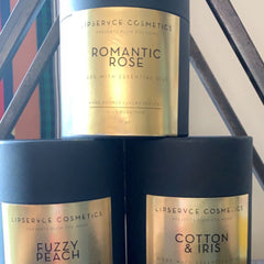 Candles with black cylindrical containers and gold labels, LIPSERVCE COSMETICS brand displayed