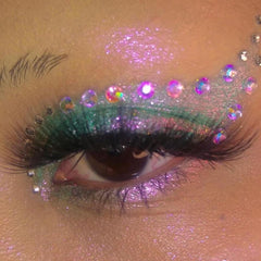 Eye makeup with green and purple glitter, and iridescent rhinestones around the eye, close up view