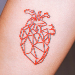 Close-up of skin-friendly red geometric heart tattoo sticker with glossy finish, shown at an angled view on hand