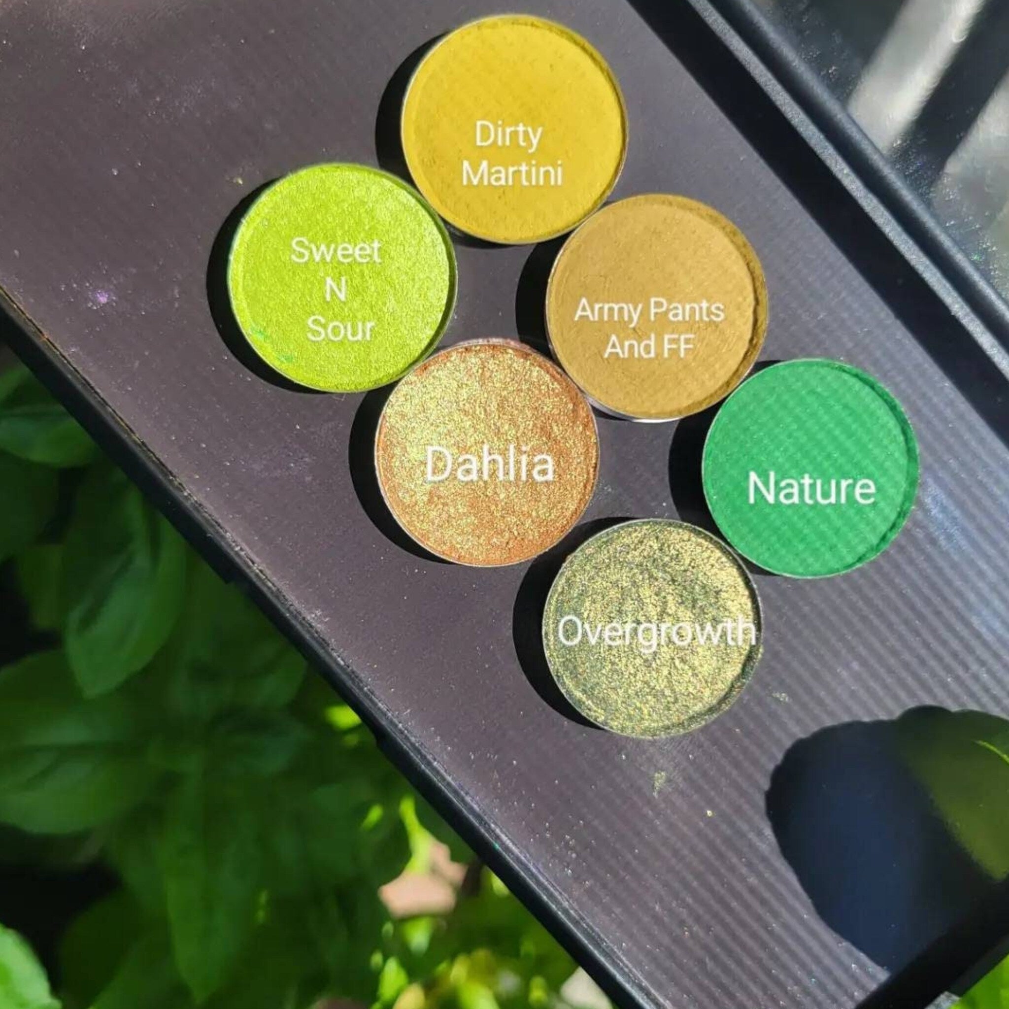 Six-pan green eyeshadow palette with earthy herb-inspired shades in matte and shimmer finishes, arranged in circular compact.