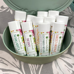 Lip balm tubes with white, printed labels in a green container on patterned fabric