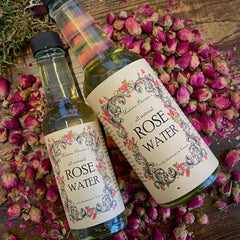 Rose water bottles with floral labels, clear glass, and black caps surrounded by rose buds