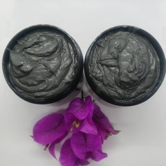 Hand applying charcoal turmeric face mask with fingertips, showing creamy dark gray texture on skin