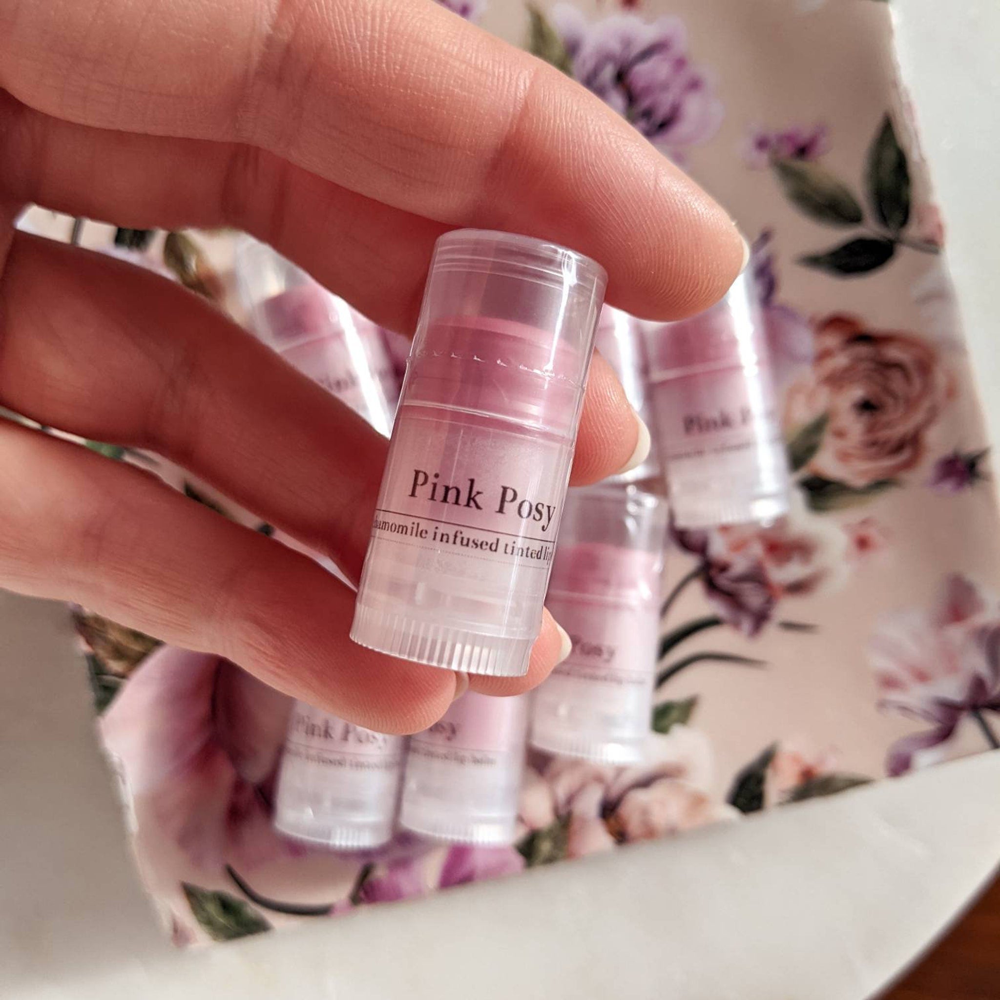 Lip balm, pink tinted tube, clear plastic, held in hand with other balms