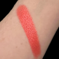 Lipstick swatch, coral color, textured finish, applied on skin