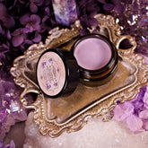 Lip balm jar with light purple balm, black rim, and Witch Beauty label on ornate gold tray