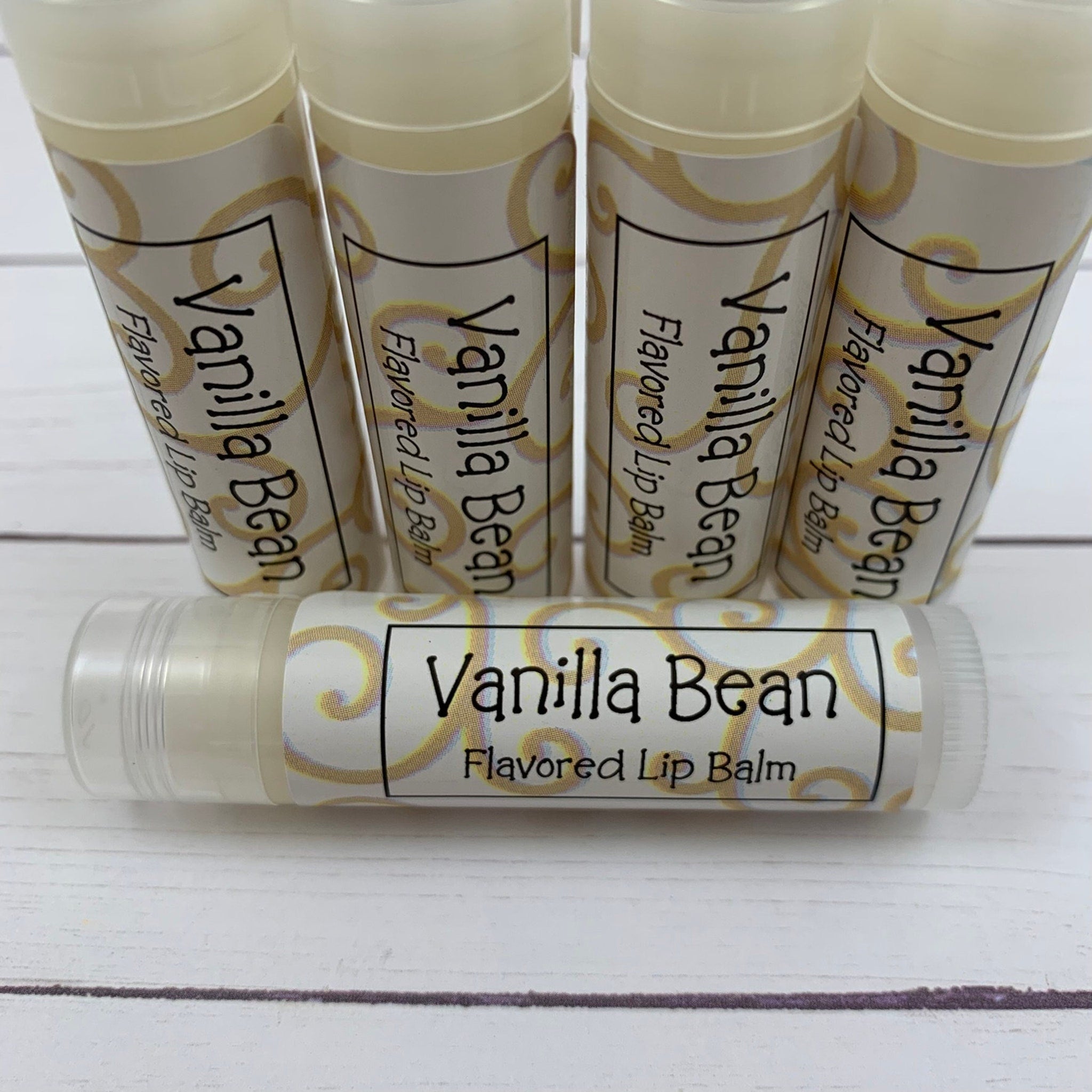 Lip balm tubes with white labels, gold swirls, and "Vanilla Bean" text