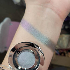 Eyeshadow swatch with iridescent green and purple hues on arm with silver compact
