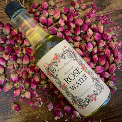 Rose water bottle with Madame Phoenix label, surrounded by pink rose buds on wood surface