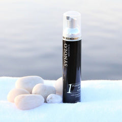 Foaming face wash bottle, black and silver, with "SYNOLO" branding and white text on a white towel