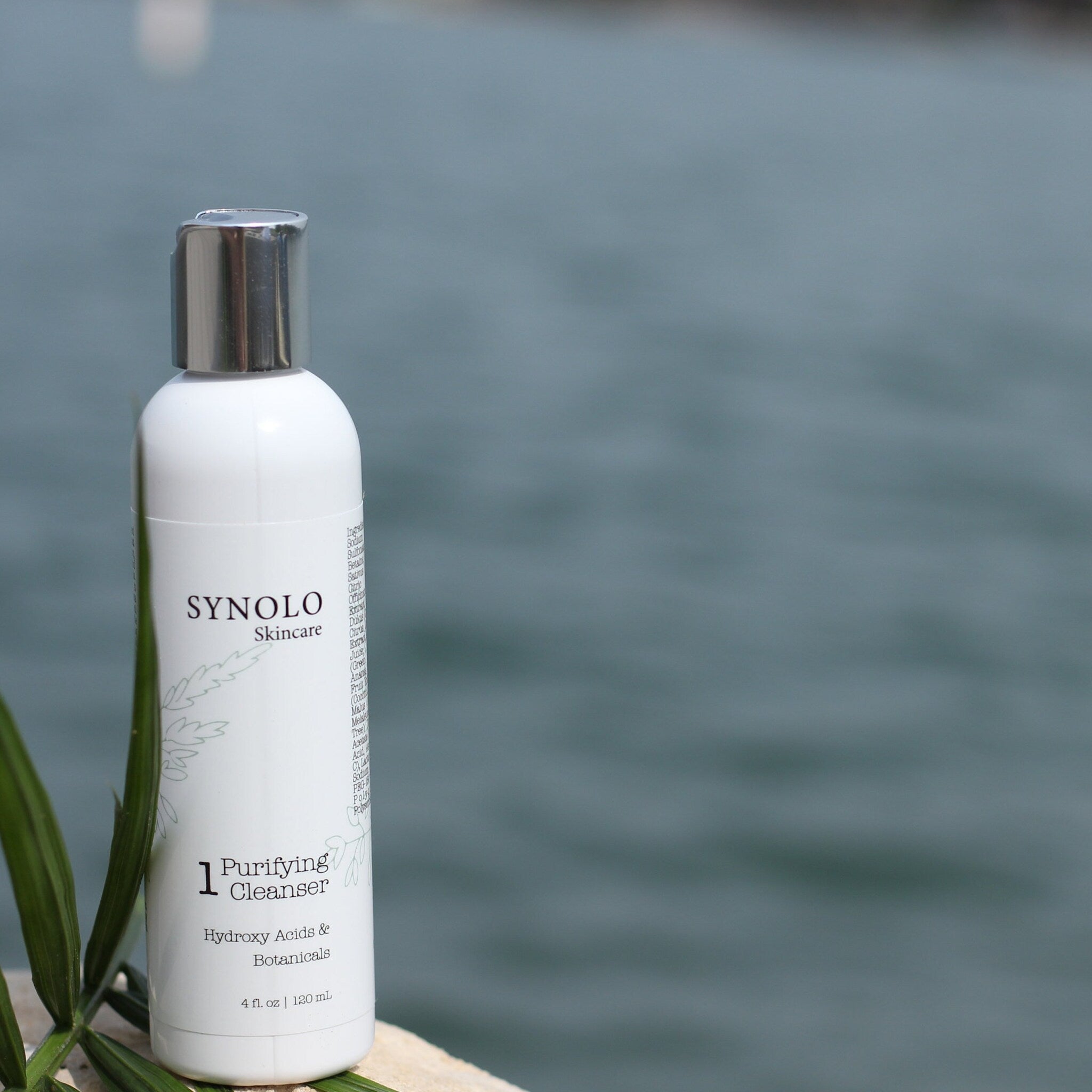 Facial cleanser bottle, white and silver with text, near water
