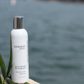 Facial cleanser bottle, white and silver with text, near water
