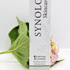 Purifying cleanser box with white and green floral design, green leaves, and pink flowers in the background