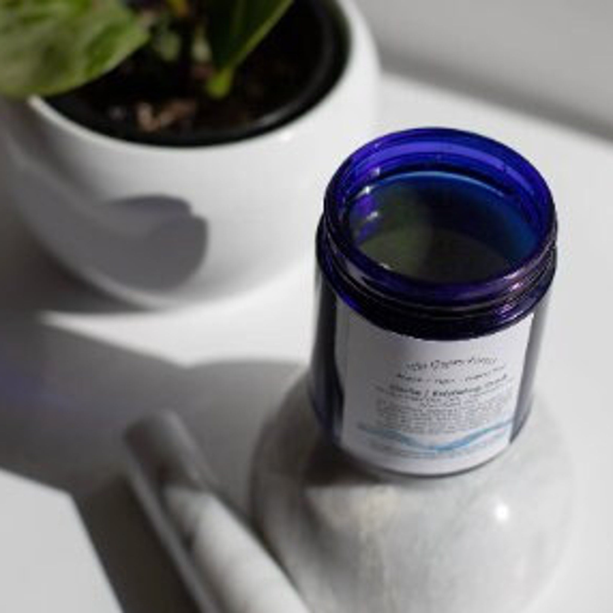 Skin care scrub jar, blue glass, white label, on white surface