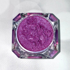 Purple glitter eyeshadow in a clear, faceted jar on white surface